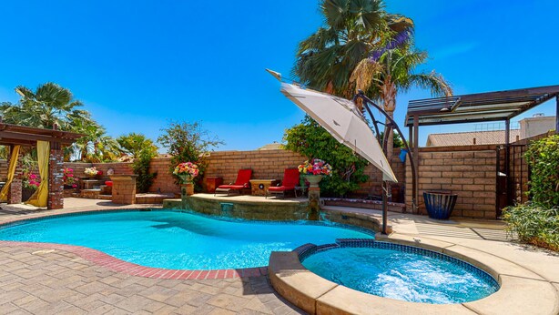 A swimming pool with a sunshade, red lounge chairs, and a brick wall. - Family-Friendly Home w/ an Outdoor Kitchen, Private Pool, & Spa - 3BR - #66708 (La Quinta)