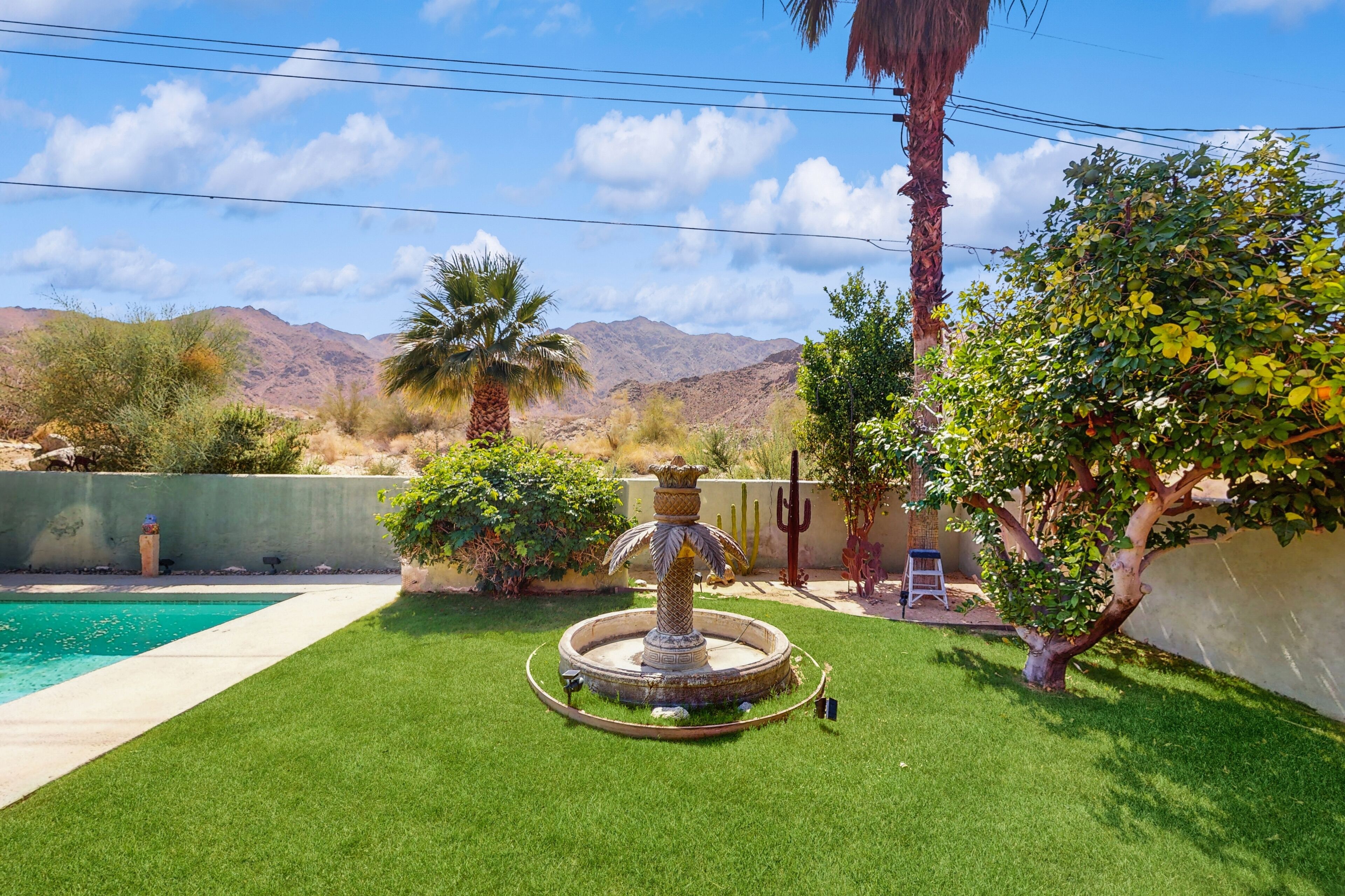 A backyard with a swimming pool, a decorative fountain, and a view of mountains.