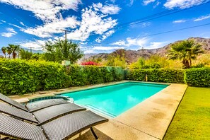 Une piscine rectangulaire à l’eau d’un bleu limpide, entourée d’une haie bien entretenue et de quelques palmiers.