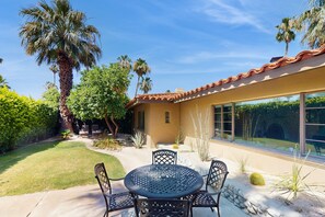 A patio with a round table and chairs, surrounded by palm trees and desert plants. - Siesta-ready home with private saltwater pool - close to downtown (Palm Springs)