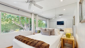 A bedroom with a bed, a ceiling fan, a nightstand with a lamp, and a TV on the wall. - Siesta-ready home with private saltwater pool - close to downtown (Palm Springs)