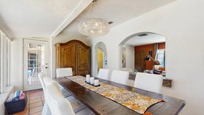 A dining area with a long wooden table, white chairs, a patterned runner, and a hanging light fixture. - Siesta-ready home with private saltwater pool - close to downtown (Palm Springs)
