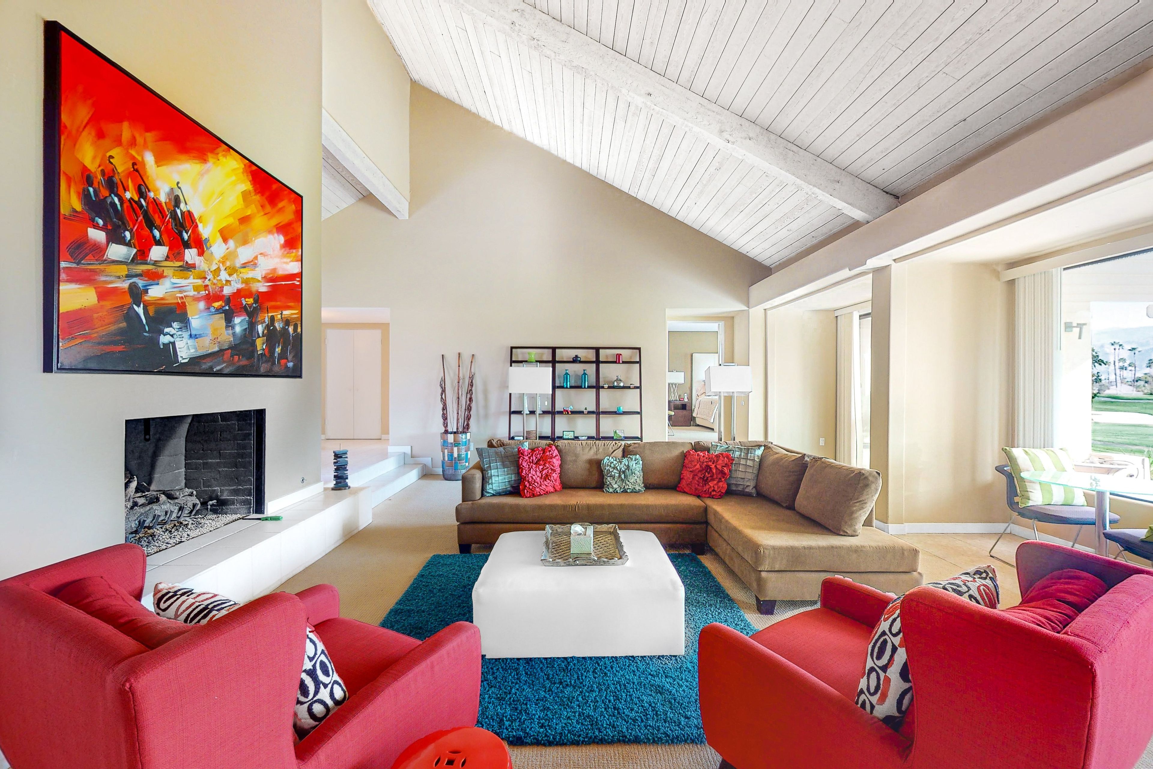 A modern living room with a sectional sofa, red armchairs, a coffee table, and a large abstract painting.
