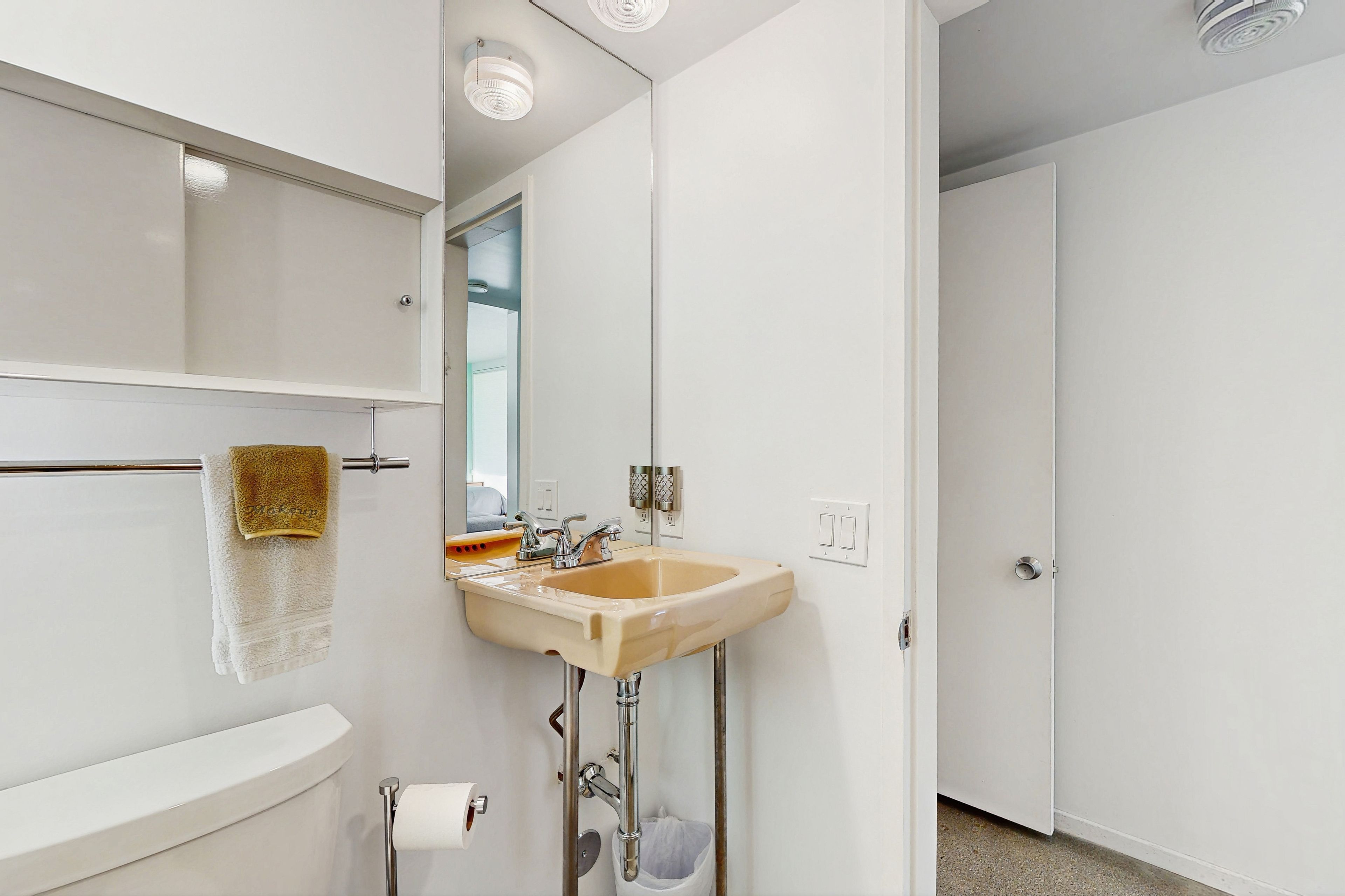 A bathroom with a white toilet, a beige sink, and a towel hanging on a towel bar.