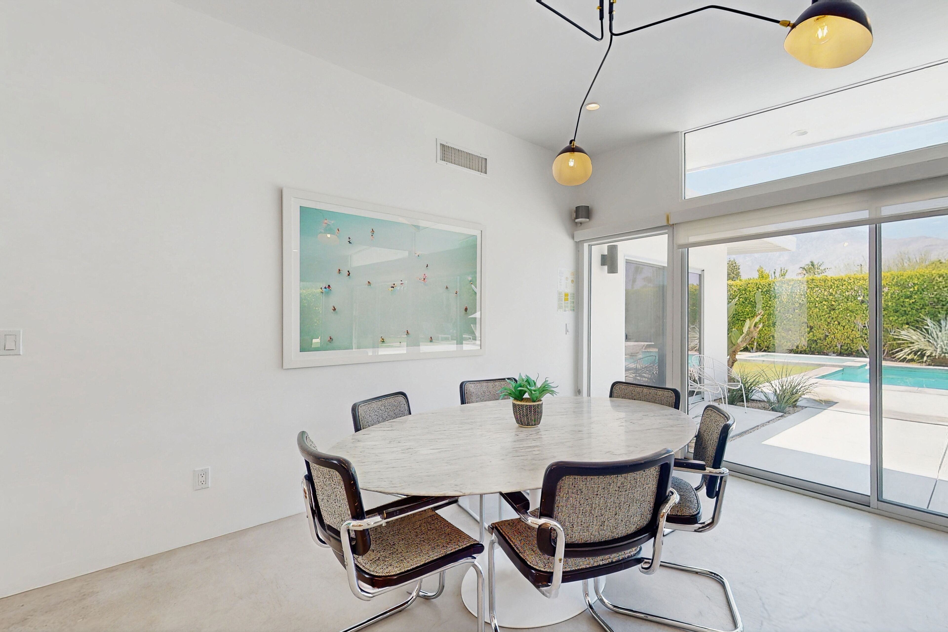 A modern dining area with a round table, six chairs, and a potted plant.