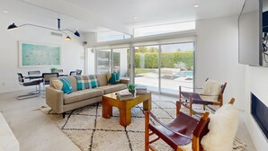 Un salon moderne avec un canapé, une table basse et des fauteuils, de grandes fenêtres et une vue sur l’extérieur.
