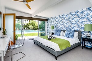 A modern bedroom with a large bed, a desk, and a view of a pool and greenery. - Fabulous Alexander home in the best neighborhood w/ pool, spa & mountain views (Palm Springs)