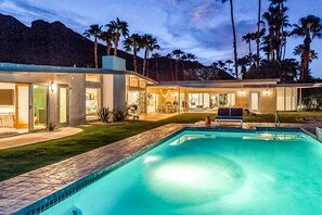 Una casa moderna con piscina, mobiliario de exterior y palmeras.