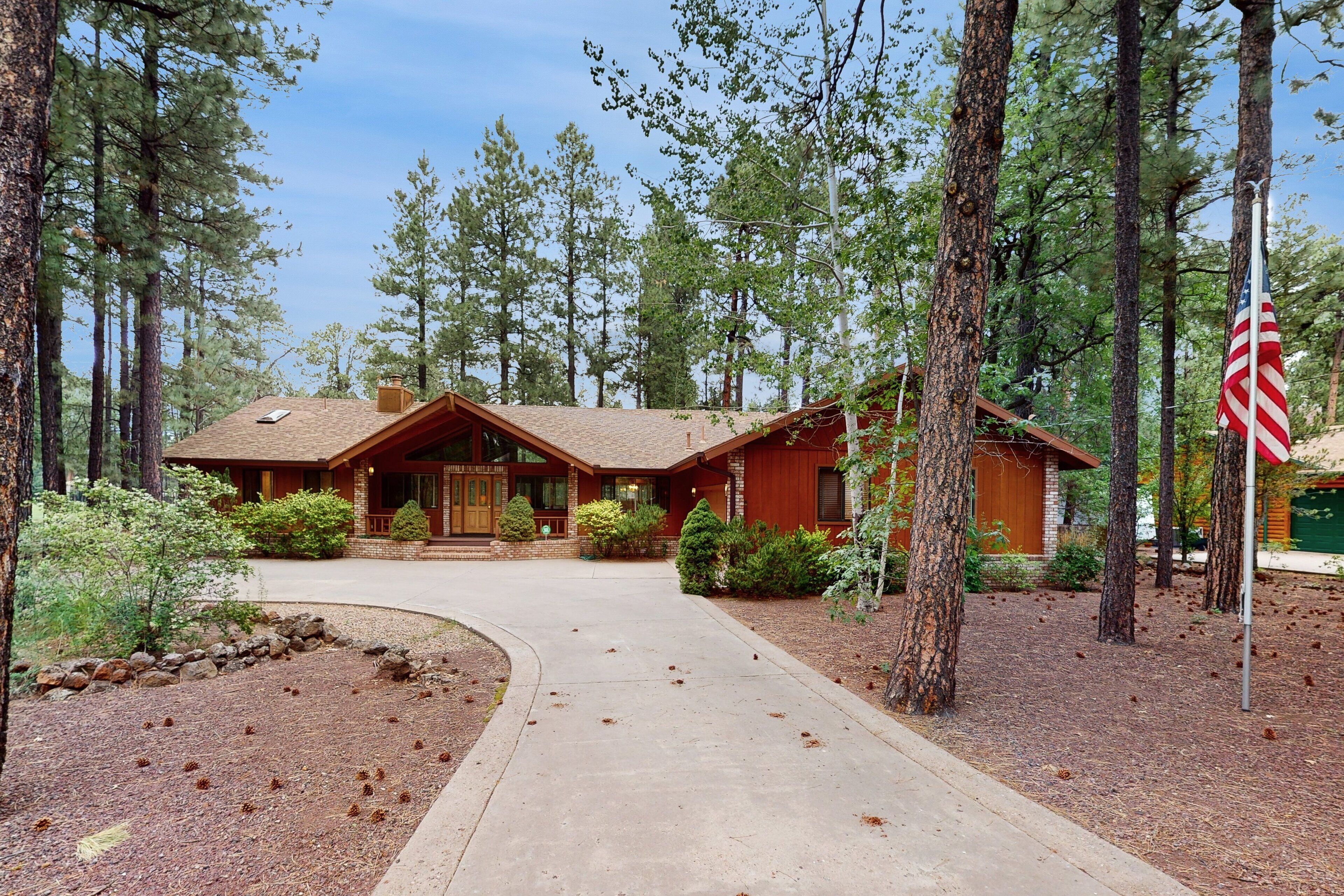 A wooden cabin with a front porch, surrounded by trees and a flag.