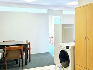 Une cuisine de taille réduite comprenant une table, des chaises, un lave-linge et un meuble en bois.