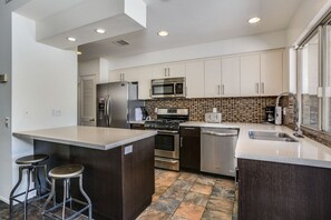 A modern kitchen with stainless steel appliances, a large island with bar stools, and a tiled backsplash. - Airy, dog-friendly home with private pool, spa, & firepit - close to town (Palm Springs)