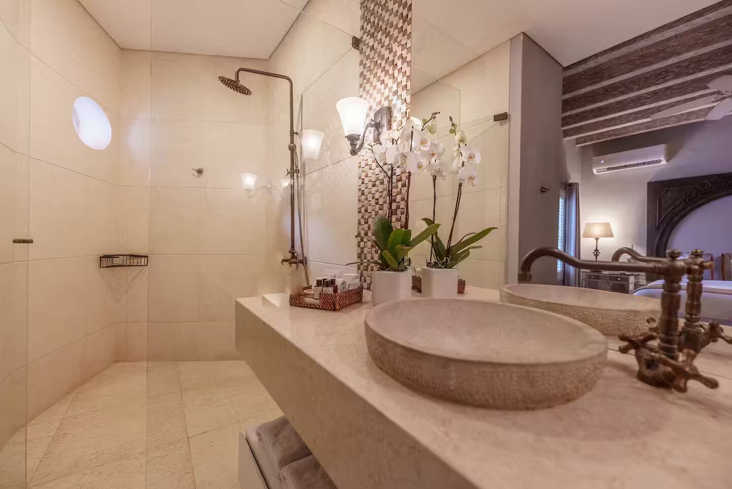 A modern bathroom with a large mirror, a round sink, a shower, and decorative plants.