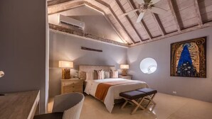 Quarto com cama, mesas de cabeceira, uma cadeira, ventoinha no teto, janela e um quadro na parede.
