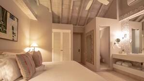 A bedroom with a bed, a nightstand, a lamp, a wardrobe, and a bathroom with a mirror and sink. - HOTEL NOI 1860: LUXURY HOUSE CARTAGENA DE INDIAS - King bed (Cartagena de Indias)