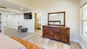 A bedroom with a wooden dresser, a large mirror, a bed with a patterned bedspread, and a view of the outside through a window. - A stately luxury house with pool nestled in a serene neighborhood (Scottsdale)