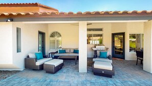 A covered patio area with outdoor furniture, a grill, and a view into the house. - A stately luxury house with pool nestled in a serene neighborhood (Scottsdale)