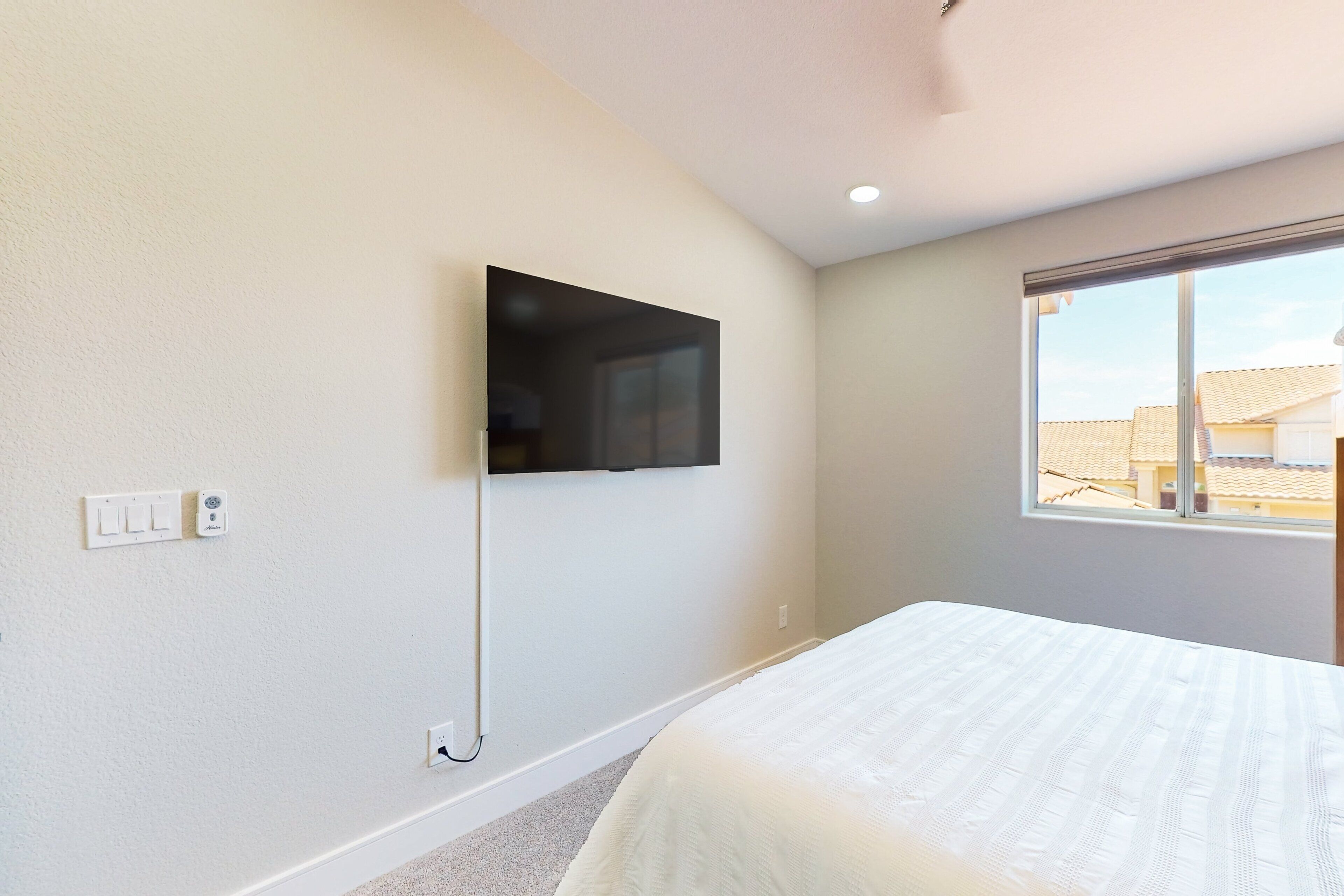 A bedroom with a bed, a wall-mounted TV, and a window.
