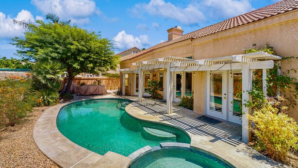 Ein Schwimmbecken mit Pergola, Baum und Gebäude mit Ziegeldach.