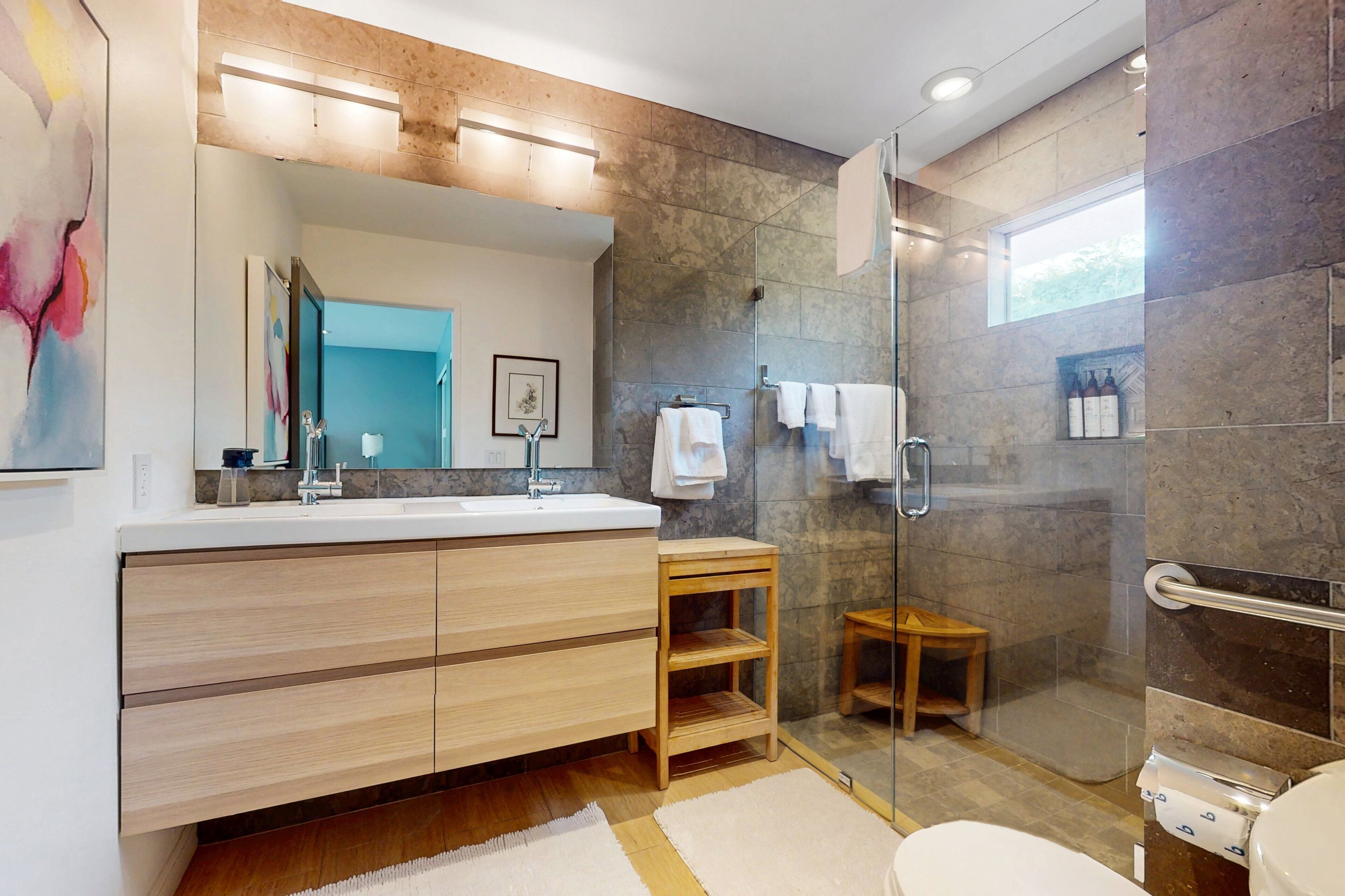 Een moderne badkamer met een grote spiegel, een houten wastafelmeubel, een douchecabine met glazen wanden en een toilet.