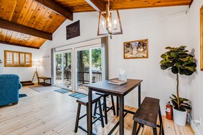 Una habitación con piso de madera, una mesa, taburetes de bar, un banco, una planta en maceta y un extintor.
