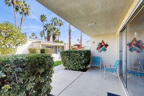 A covered outdoor area with a glass door, a hedge, and a blue chair. - Delightful and sophisticated condo with shared tennis, outdoor pool, & spa (Palm Springs)