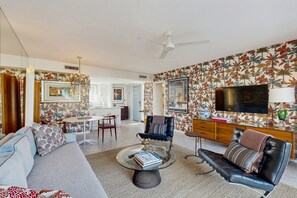 A modern living room with a sofa, armchair, and coffee table. There is a dining area with a table and chairs, and a kitchen in the background. - Delightful and sophisticated condo with shared tennis, outdoor pool, & spa (Palm Springs)