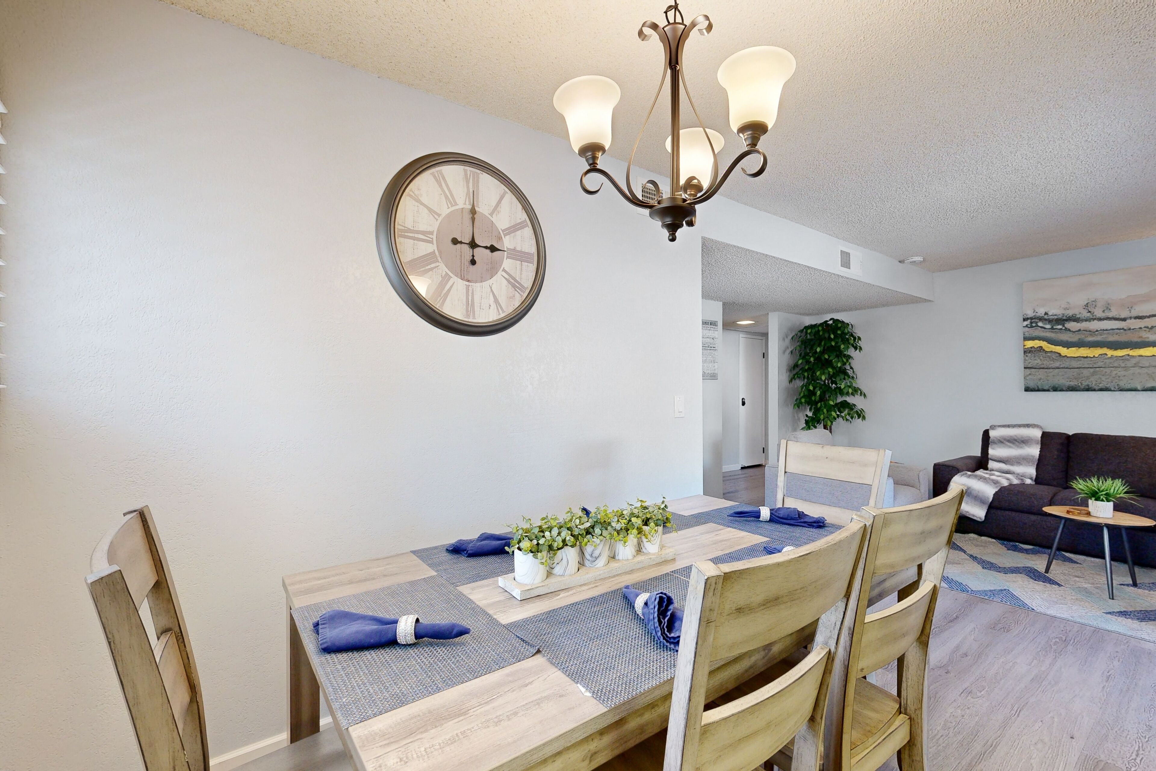 Un coin repas avec une table en bois, des chaises, un lustre et une horloge murale.