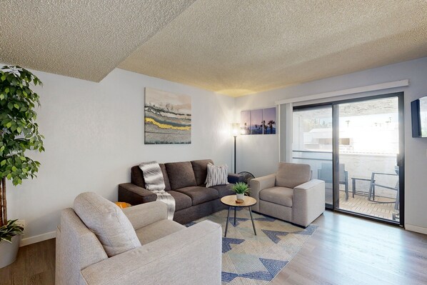A modern living room with a sofa, armchairs, a coffee table, and a large window. - Lovely Palm Tree Retreat with Pools, Hot Tubs & Tennis | Near Golf & Dining (Palm Springs)