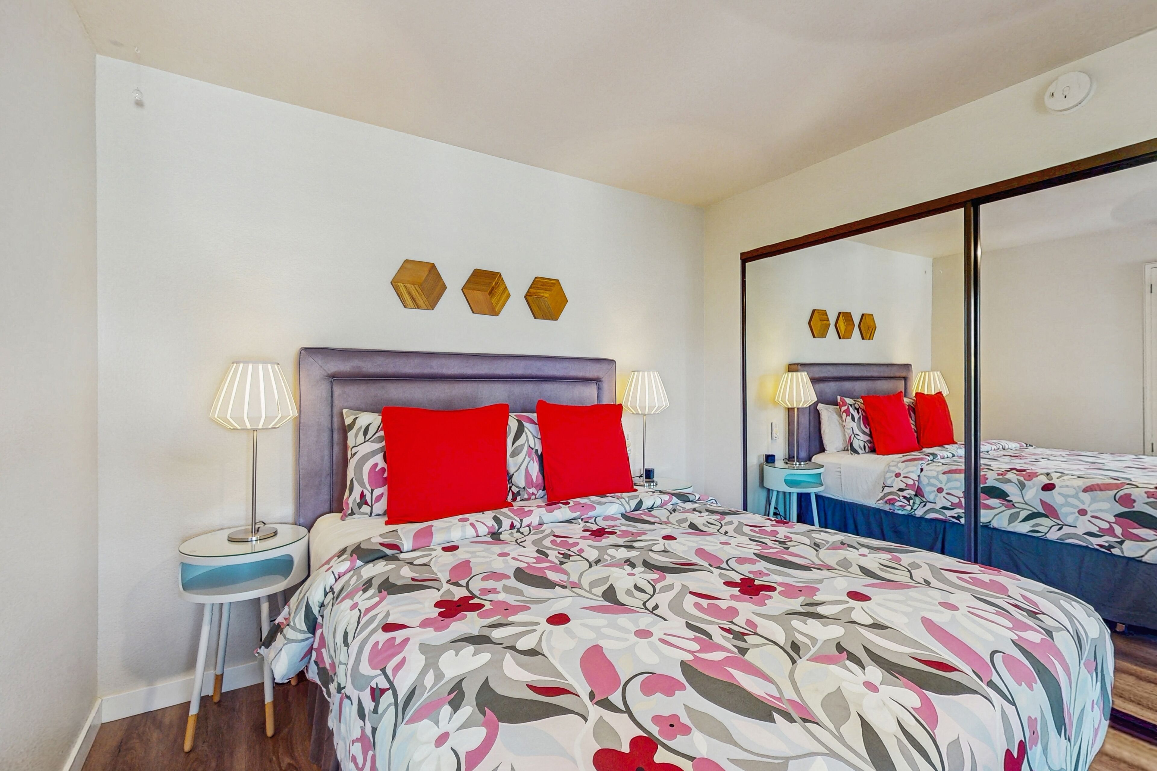 A hotel room with a large bed, two bedside tables, a mirror, and a wall-mounted light fixture.