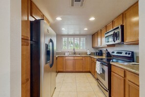 A kitchen with wooden cabinets, a stainless steel refrigerator, a microwave, an oven, and a sink.
