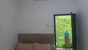 A bedroom with a bed, an air conditioning unit, and a view of greenery through an open door. - OYO 95184 Ms Home Syariah (Tegal)