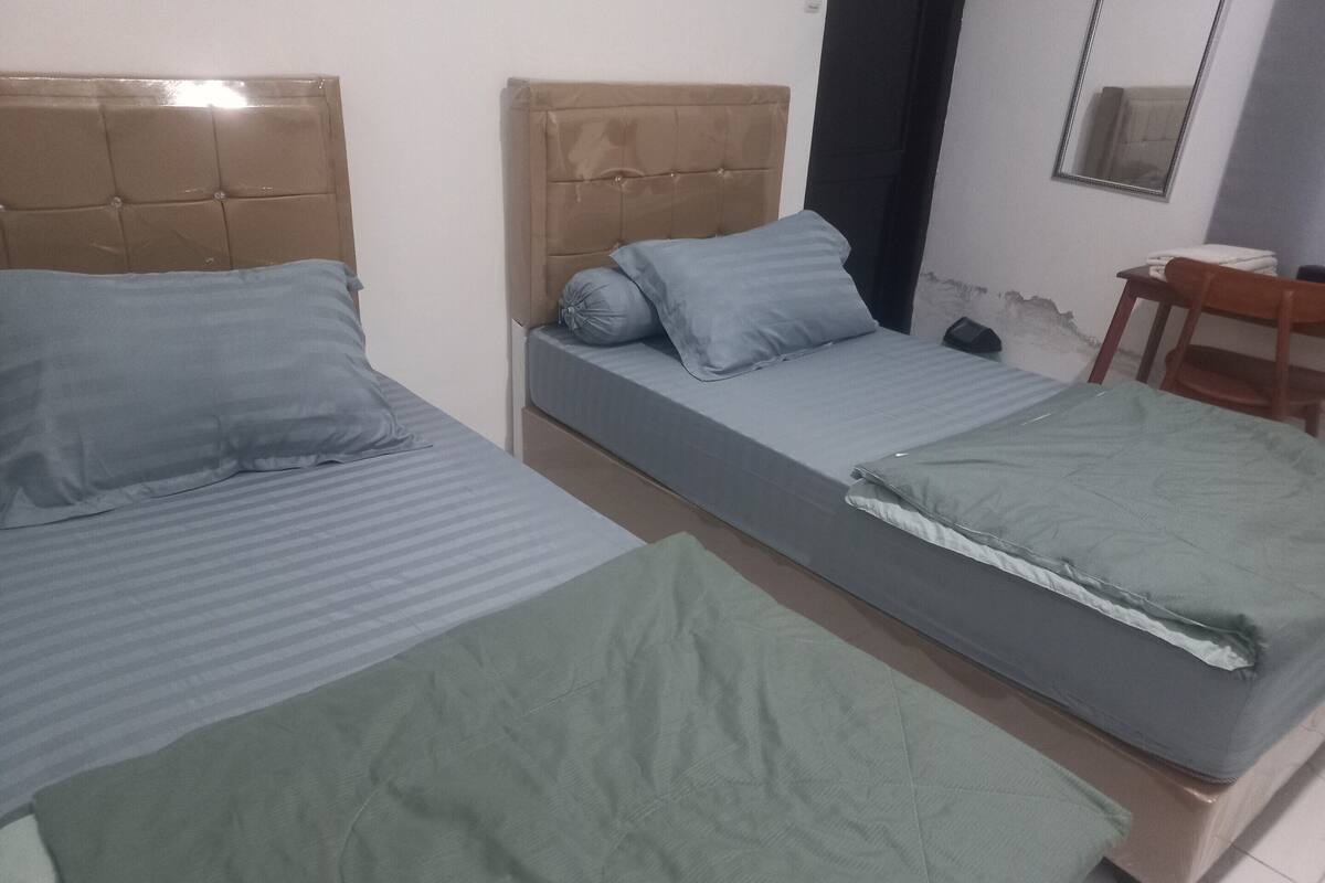 A room with two beds, each with a headboard and pillows. There is a chair and a small table in the corner.