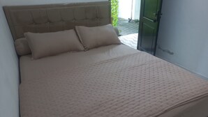 A bed with a tufted headboard and two pillows, a green door, and a tiled floor. - OYO 95184 Ms Home Syariah (Tegal)