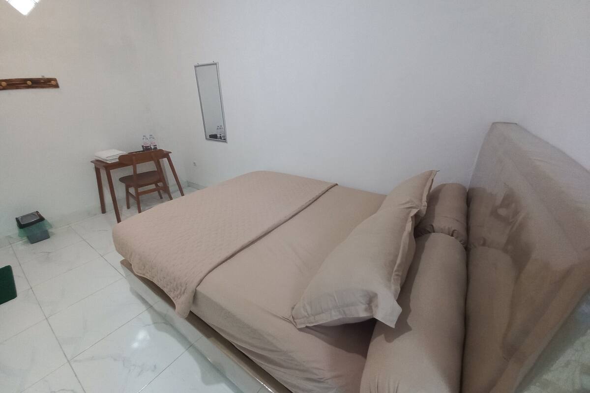 A bedroom with a bed, a chair, a small table, and a mirror on the wall.