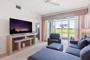 A living room with a flat-screen TV, a ceiling fan, a large window with curtains, and a view of a golf course. - 1315 - First-Floor Green Links with Golf Views (Naples)