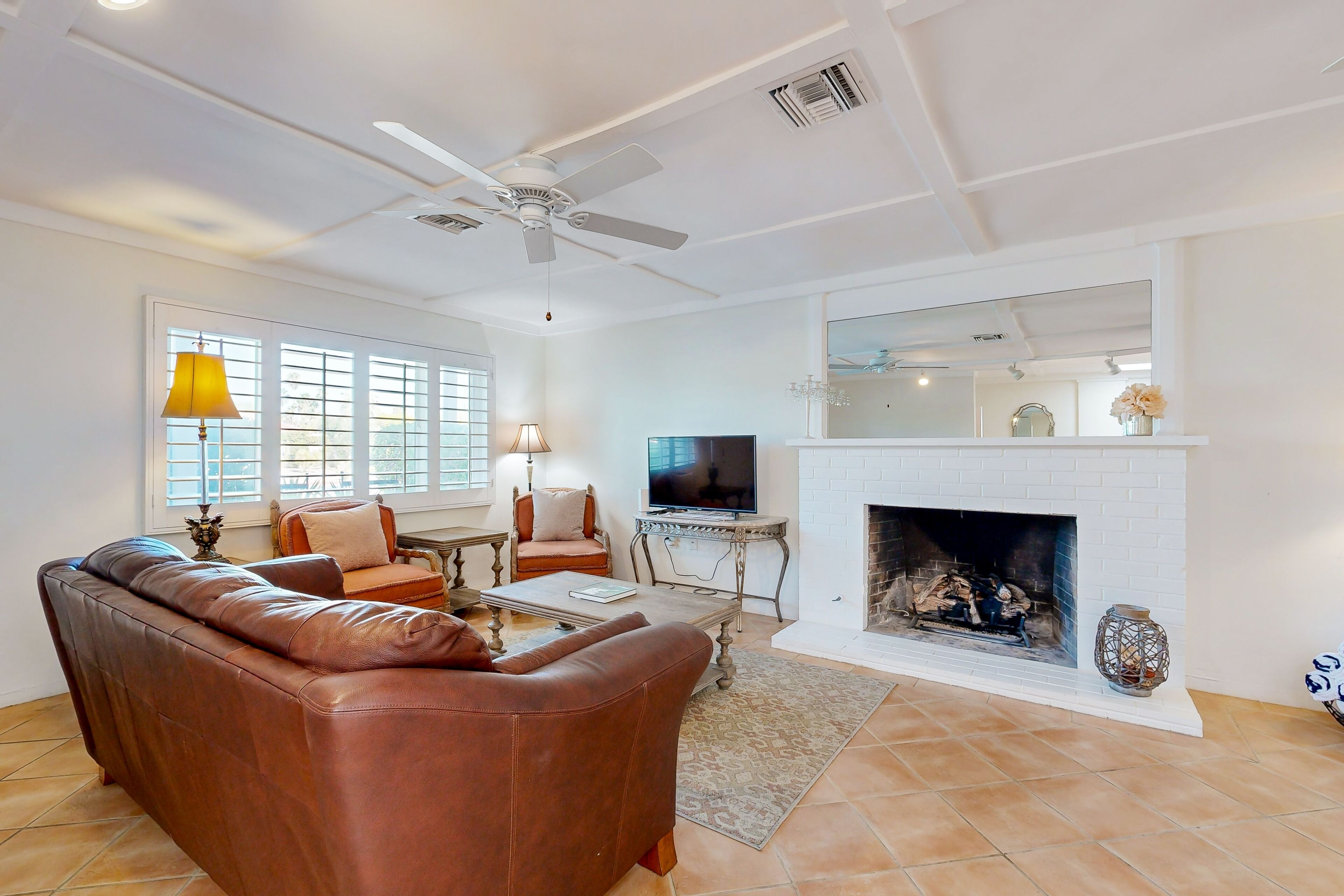 A living room with a brown leather sofa, a television on a stand, a fireplace, and a ceiling fan.