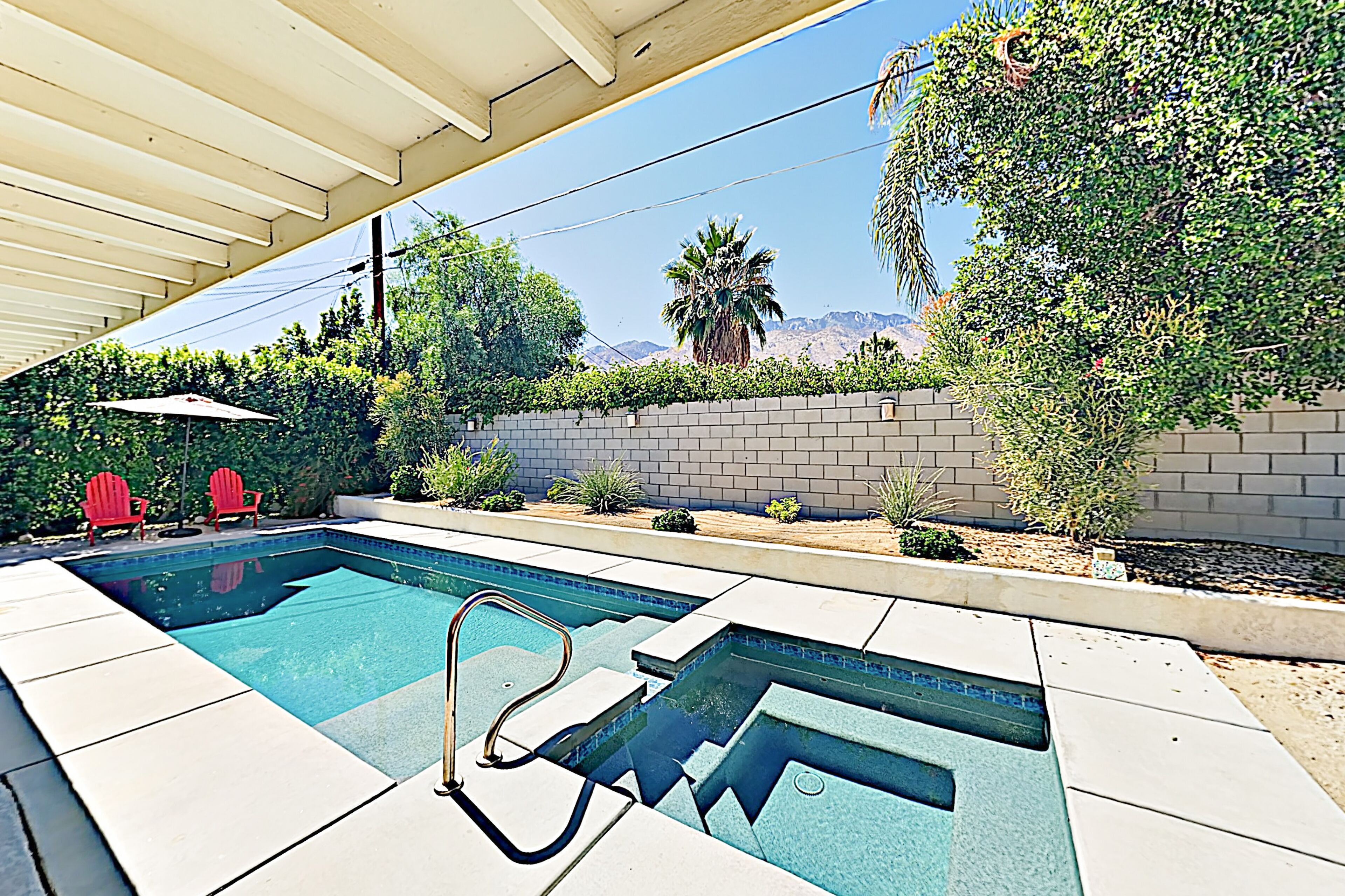 A swimming pool with a diving board, red chairs, and a covered patio area.