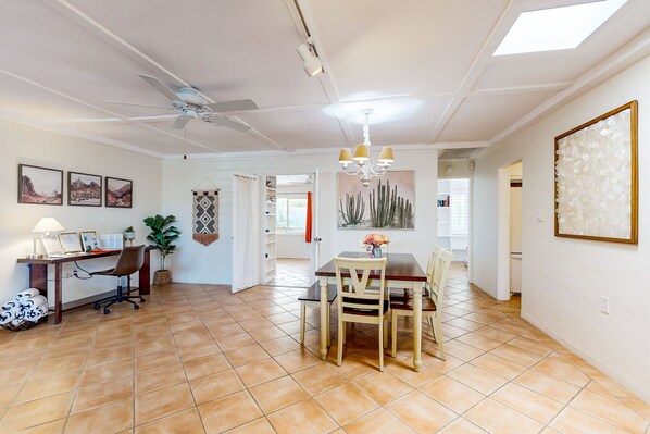 Un vaste espace de vie comprenant une table à manger, des chaises, un bureau avec un ordinateur et un ventilateur de plafond.
