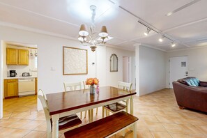 Un coin repas avec une table et des chaises en bois, un lustre et une cuisine en arrière-plan.