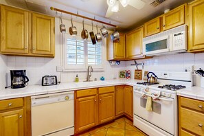 Une cuisine avec des meubles en bois, un micro-ondes blanc, une cuisinière et des casseroles suspendues.