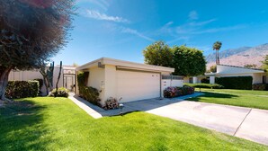 Een modern gelijkvloershuis met garage, omringd door verzorgde gazons en diverse beplanting.