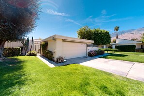 A modern single-story house with a garage, surrounded by well-maintained lawns and a variety of plants. - Convenient, dog-friendly condo w/shared tennis, spa, heated pool (Palm Springs)
