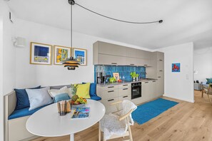 Una cocina moderna con salpicadero azul, un comedor con mesa redonda y una zona de estar con sofá.
