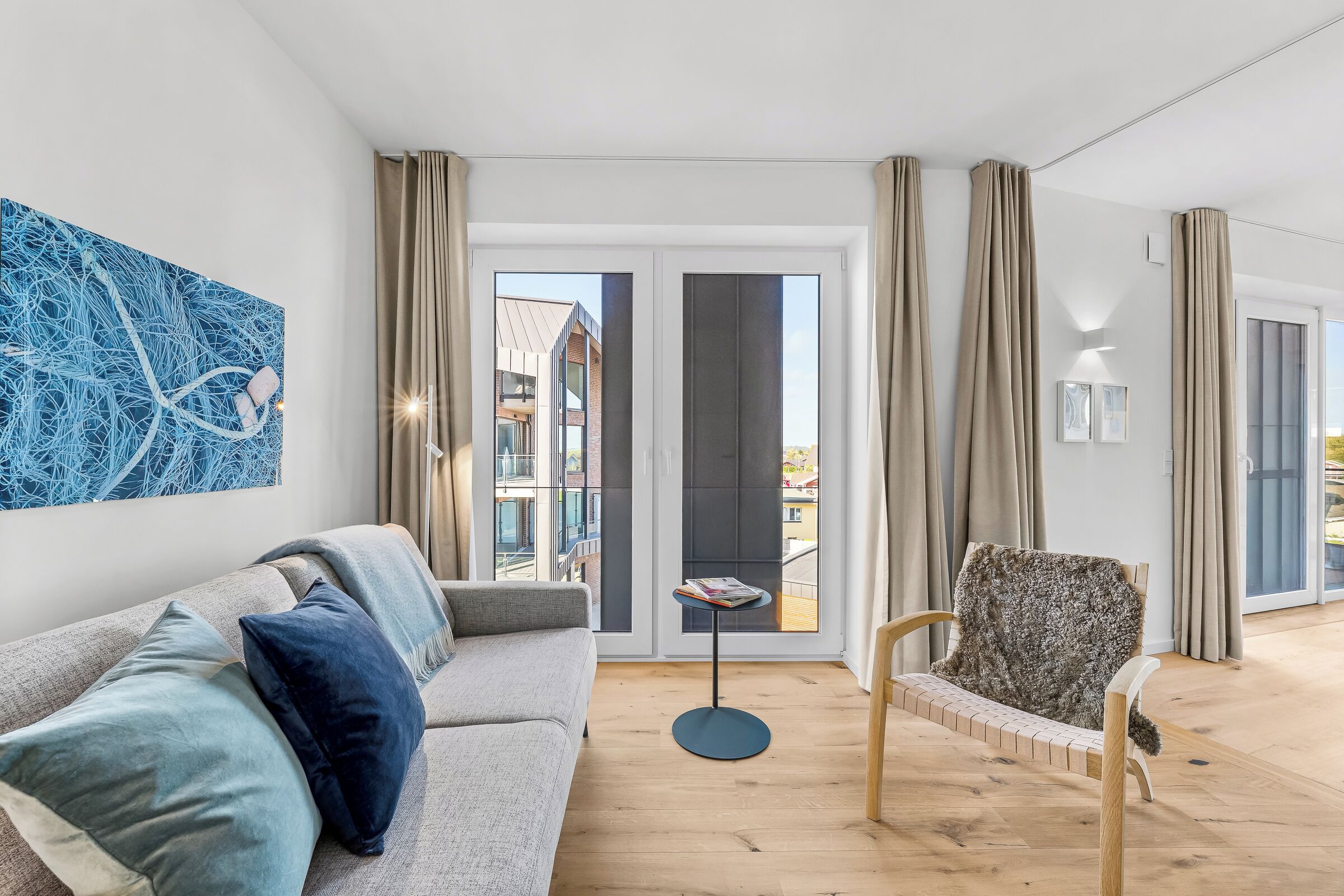 Un salon moderne avec un canapé, un fauteuil à motifs, une table basse et une grande fenêtre avec des rideaux.