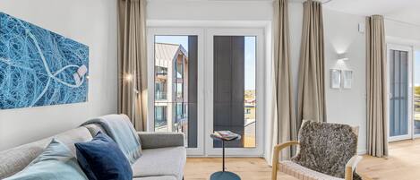 Un salon moderne avec un canapé, un fauteuil à motifs, une table basse et une grande fenêtre avec des rideaux.