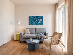 A modern living room with a grey sofa, a round coffee table, a wooden chair, and a large window with curtains. - The View B13 Fain Leewen - Balcony, elevator, shared. Sauna, parking space (Dagebüll)