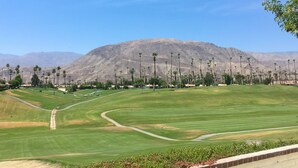Ein Golfplatz mit Bergpanorama, gepflegtem Rasen und Palmen.