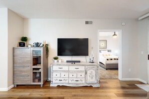 A living room with a TV, a white cabinet with drawers, a small plant, and a bed in the background. - Ground-floor condo with on-site pool, pickleball, hot tub, gym & private balcony (Chandler)