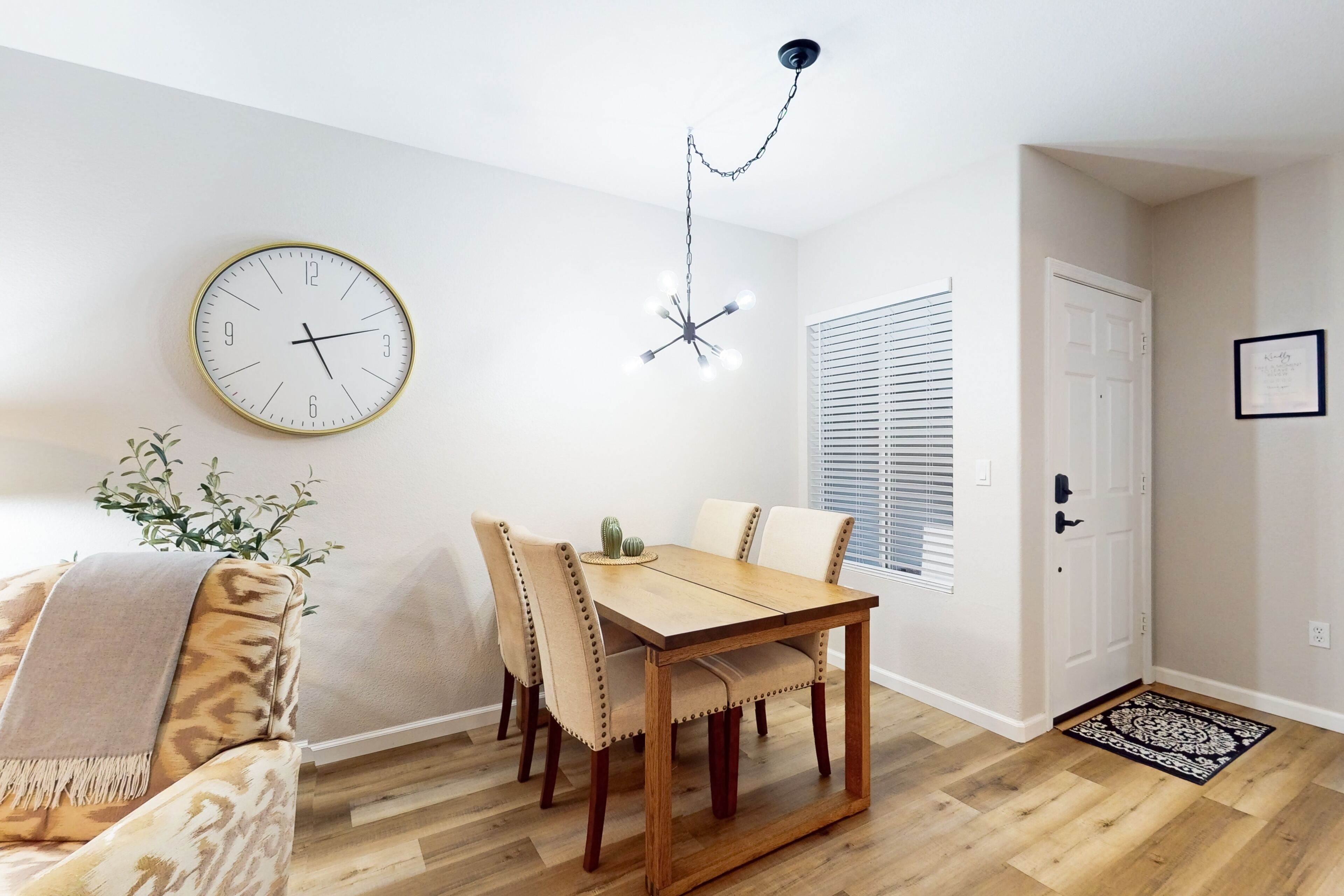 A dining area with a wooden table, beige upholstered chairs, a wall clock, and a hanging light fixture.