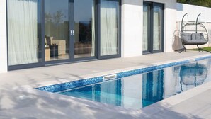 Una casa moderna amb piscina, portes corredisses de vidre grans i un pati amb mobles d'exterior.